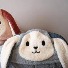 Two plush bunny hats, one pink and one gray, on a light surface with a neutral background.

