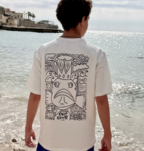 Person wearing a white t-shirt with a black graphic design on the back, standing by the water.