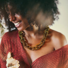 Woman wearing a red knitted garment with a necklace, surrounded by flowers.

